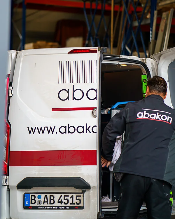 Ein Mitarbeiter in abakon-Jacke am geöffneten Heck eines beschrifteten abakon-Transporters.