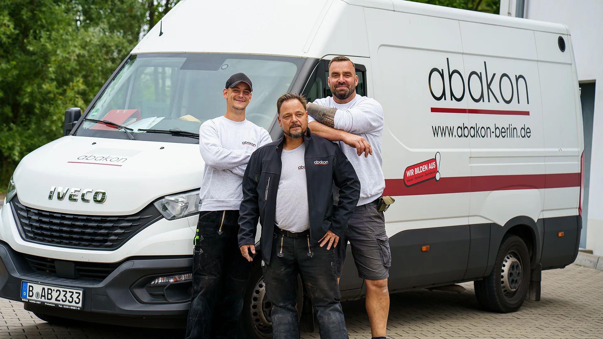 Drei Mitarbeiter von abakon stehen vor drei Firmentransportern, dahinter das Firmengebäude mit abakon-Schriftzug.